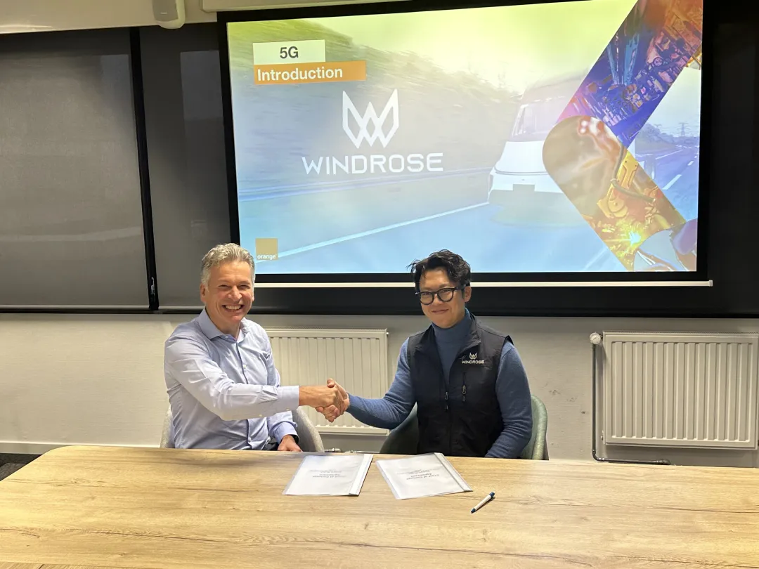 Executives from Orange and Windrose shaking hands after signing the 5G V2X partnership agreement, with a Windrose introduction slide on screen behind them